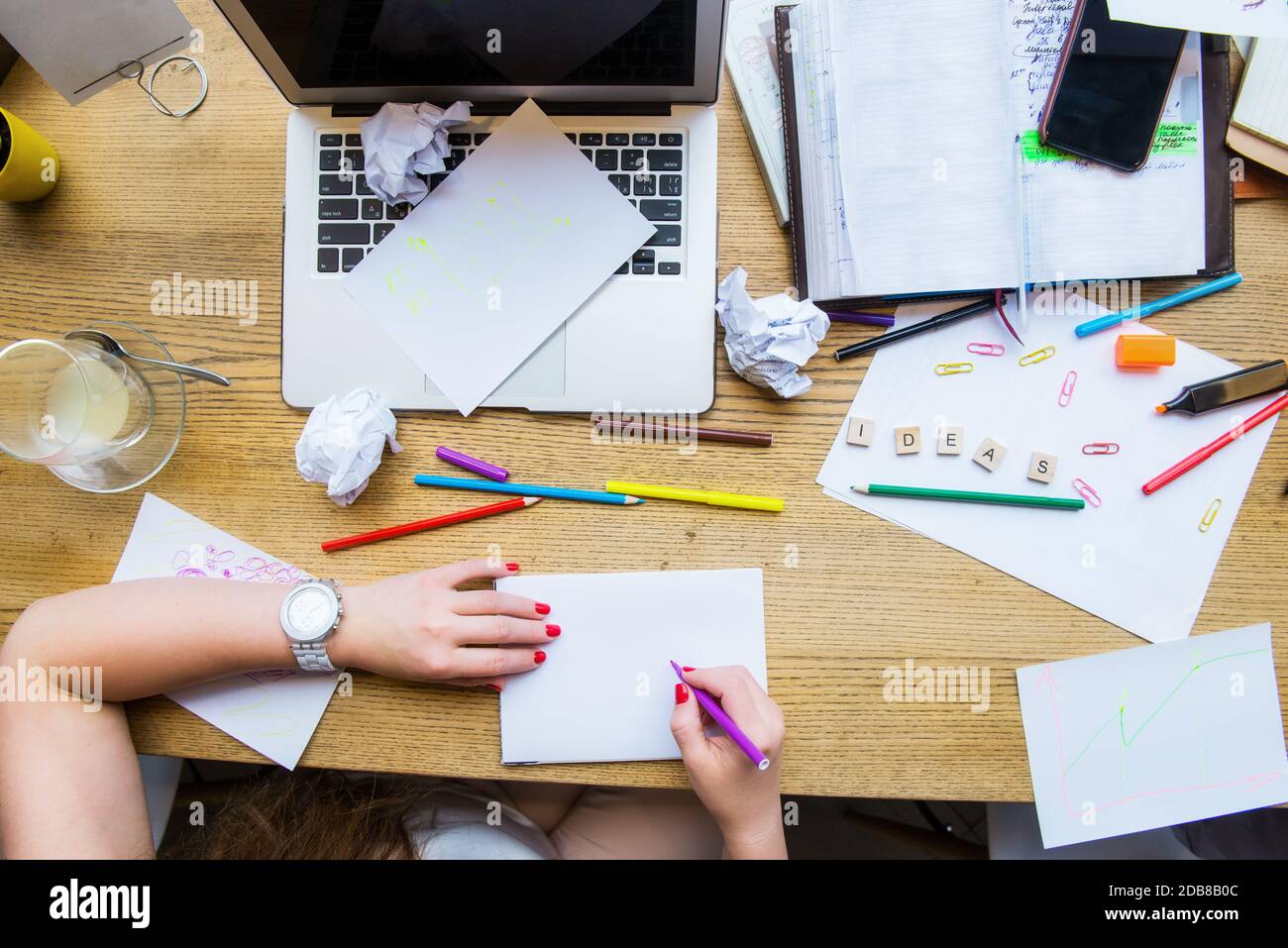 Draufsicht weibliche Hände halten Stift über weißem leeren Notizbuch für neue kreative Ideen. Arbeitsplatz mit Laptop, Rohlingen, buntem Briefpapier und Ideen Stockfoto