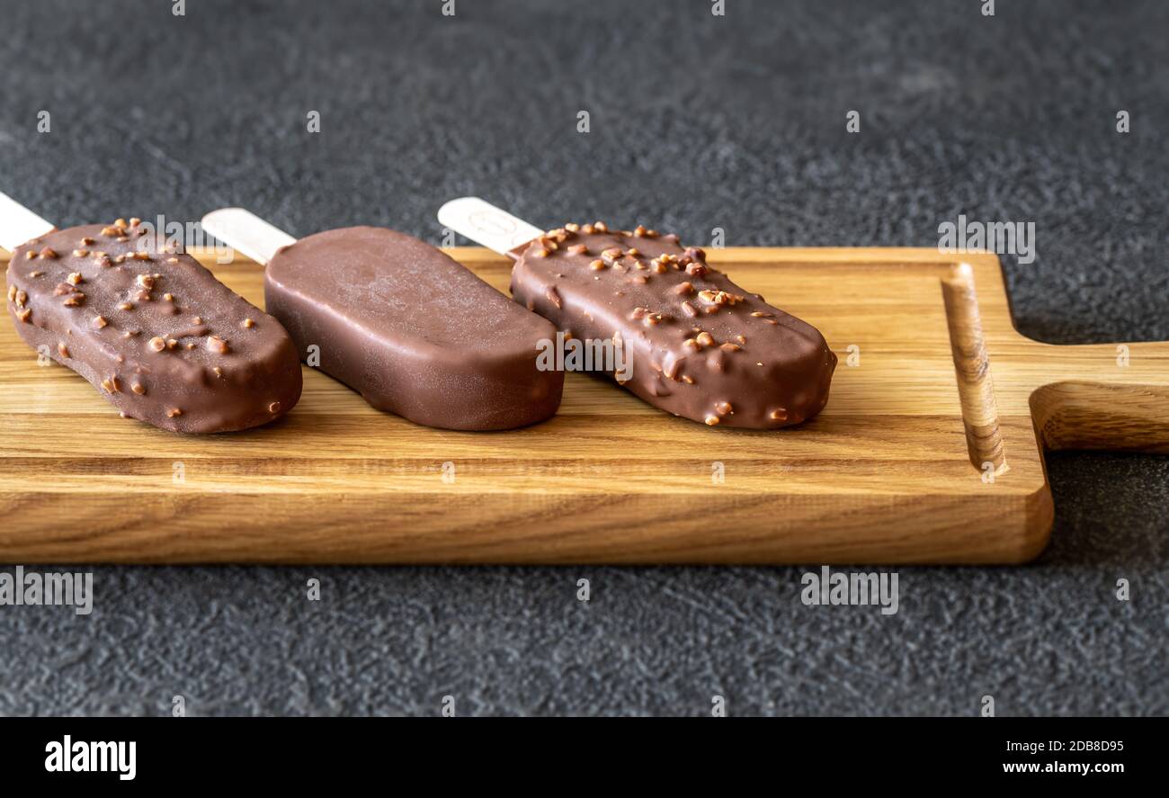 Schokoladenbedeckte Vanilleeissägel auf dem Holzbrett Stockfoto