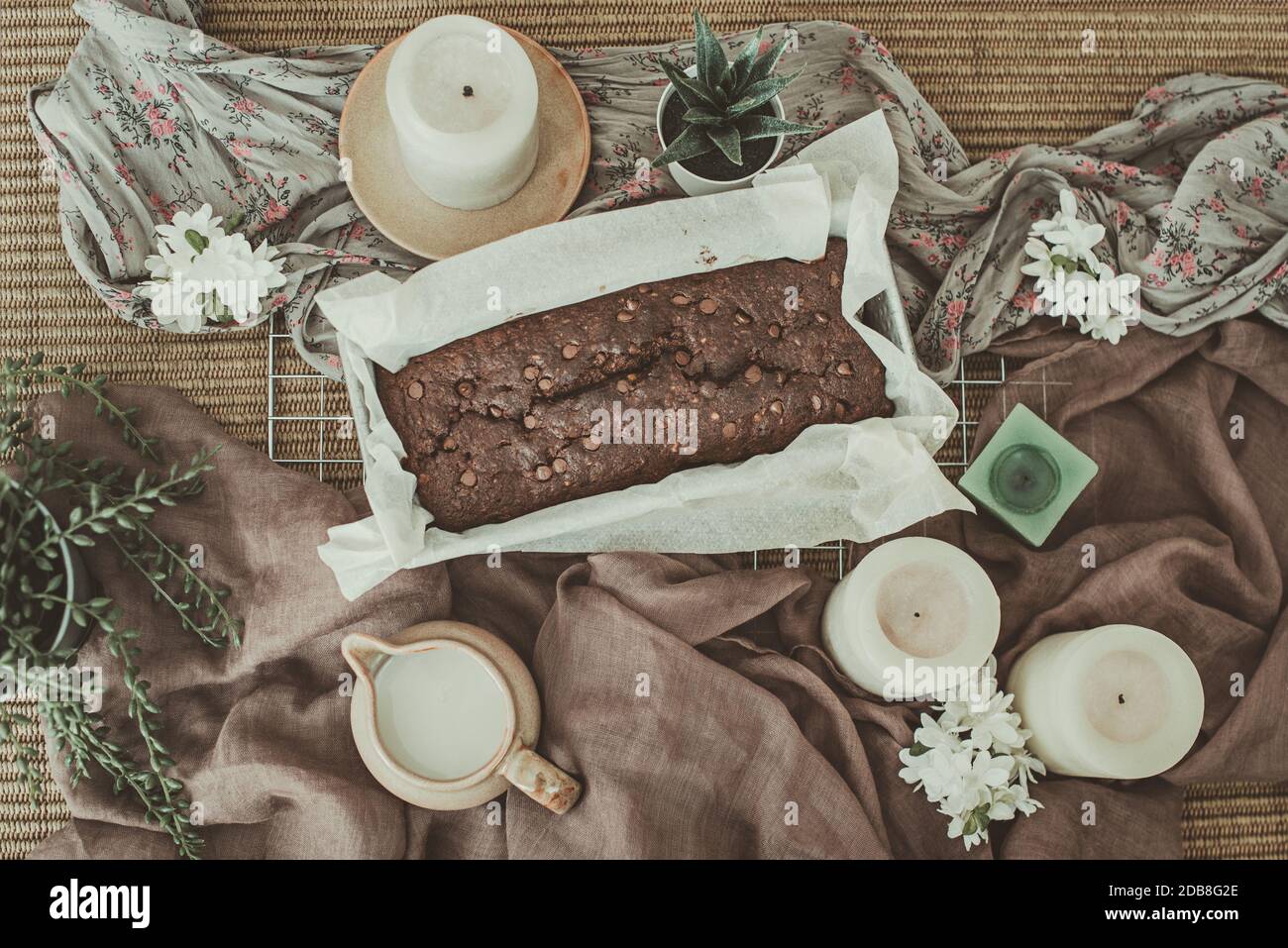 Blick von oben auf Schokoladenkuchen mit Kerzen, Pflanzen und einem Topf Sahne Stockfoto