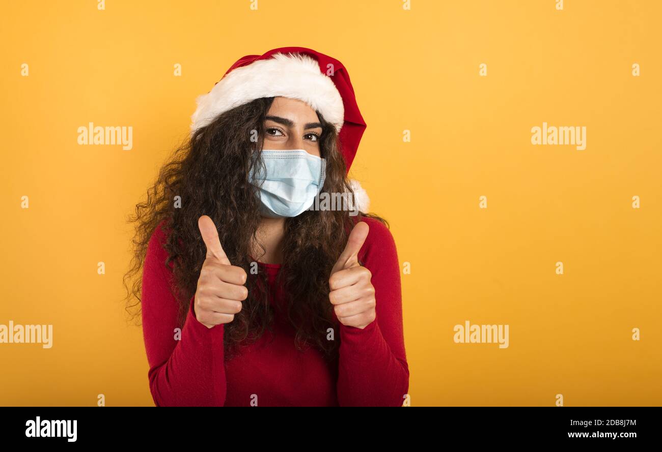 Frau mit Weihnachtshut ist optimistisch über die Niederlage der covid 19 Coronavirus. Gelber Hintergrund. Stockfoto