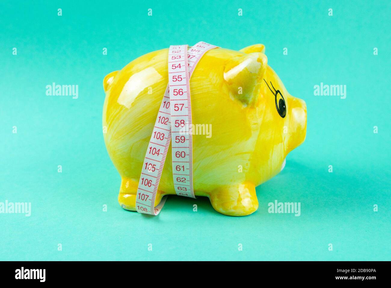 Gelbes Sparschwein in Form eines Schweins, umwickelt mit Maßband auf hellgrünem Hintergrund. Das Konzept der Einsparung von Geld um wei zu verlieren Stockfoto