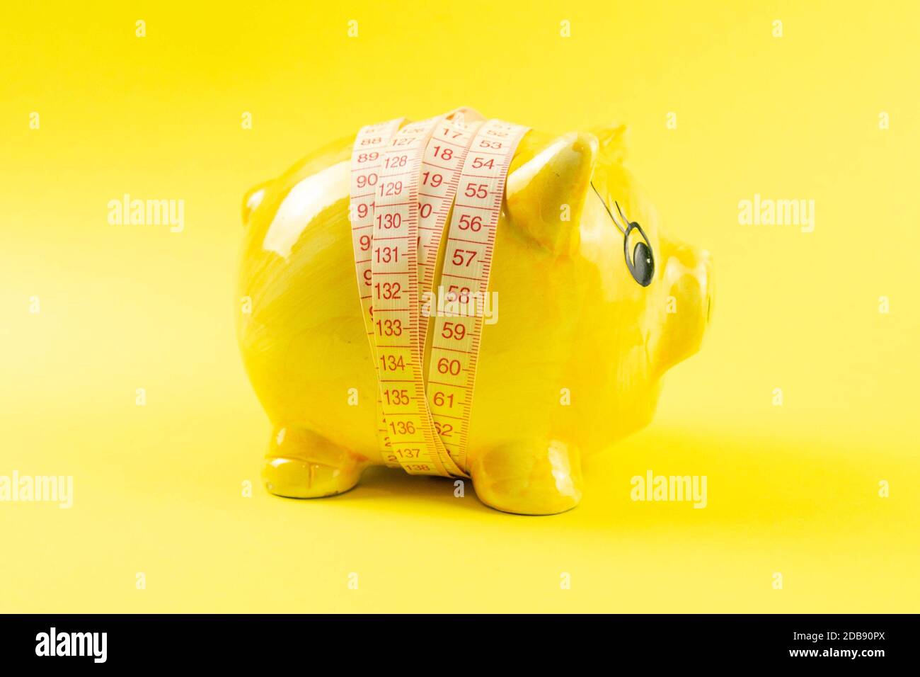 Gelbes Sparschwein in Form eines Schweins, umwickelt mit Maßband auf gelbem Hintergrund. Das Konzept der Einsparung von Geld um des Abnehens willen. Stockfoto
