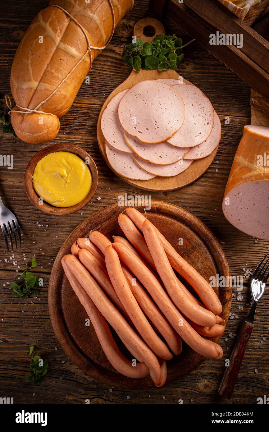 Draufsicht auf Deli-Fleischscheiben und Frankfurter Würstchen mit Senf auf Vintage-Holzhintergrund serviert Stockfoto