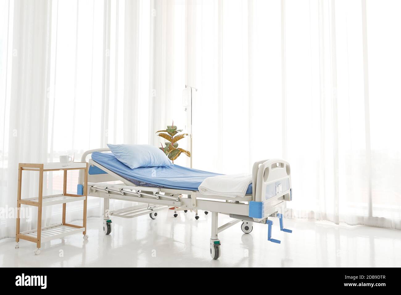 Sauberes und leeres leeres Krankenhaus in der Nähe von Sonnenfenster, blaue Bettwäsche mit weißem Vorhang im Stationsraum als Hintergrund Stockfoto