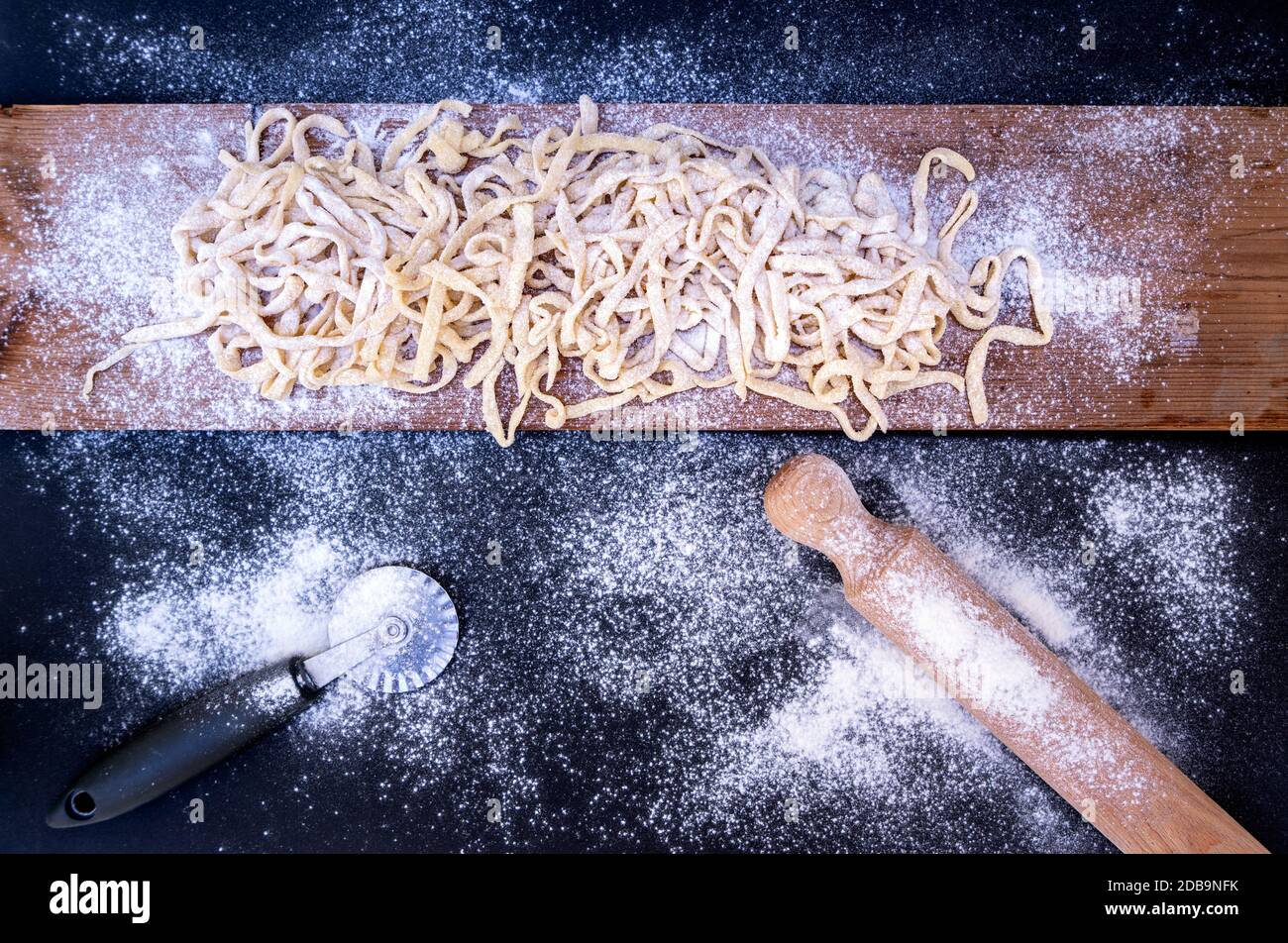 Rohe Pasta auf Holztisch mit Nudelholz und Radschneider Stockfoto