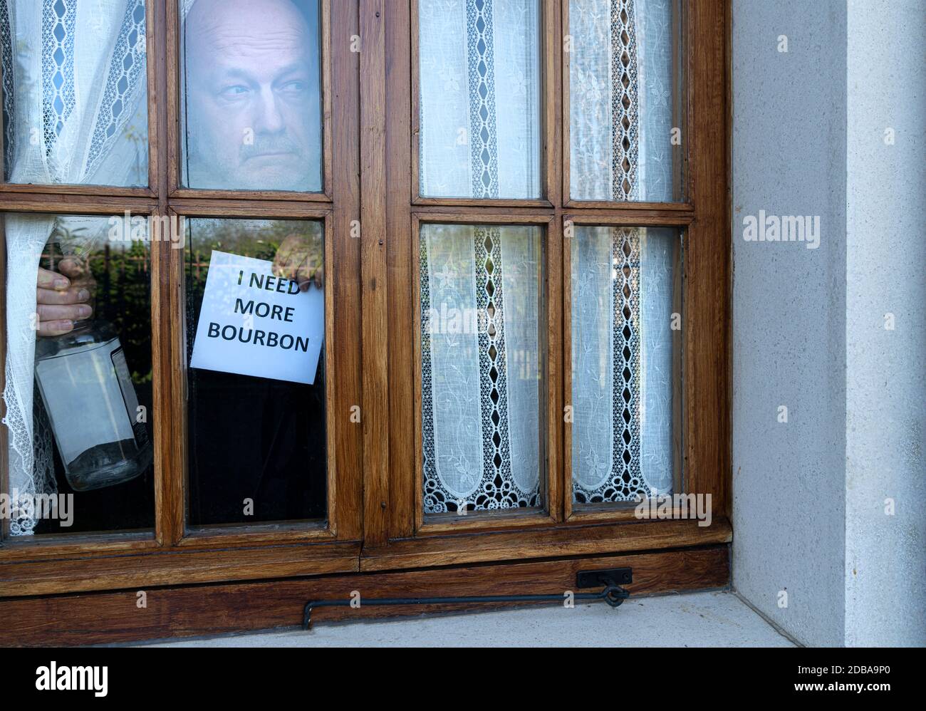 Ein Mann in Quarantäne, der mit einem Schild aus dem Fenster schaut und eine Flasche Bourbon findet Stockfoto