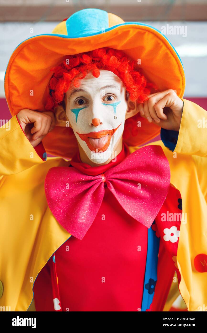 Lustige Clown mit Make-up in bunten Hut gekleidet und Kostüm Posen im Kinderbereich. Geburtstagsfeier im Spielzimmer, Babyurlaub auf dem Spielplatz. Kindisch Stockfoto