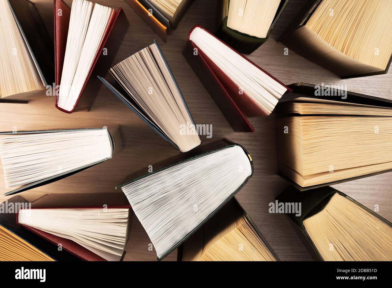 Bücher auf dem Tisch, Draufsicht. In Büchern sind die Blätter in Form eines Ventilators verteilt, die Schatten der Bücher auf einem hellen Holztisch. Zurück zur Schule. Stockfoto