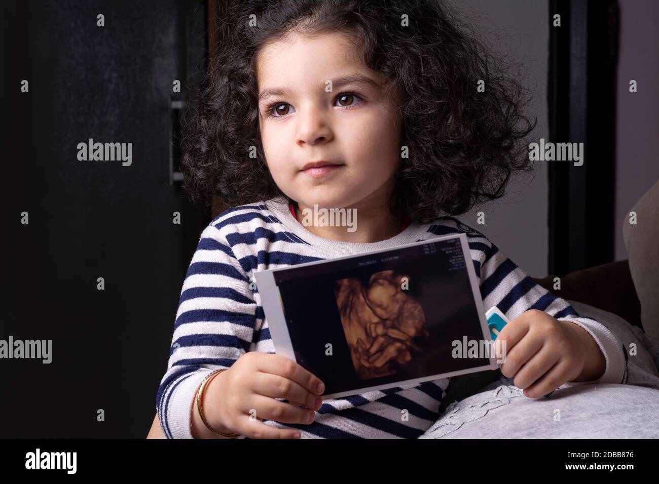Ein zwei Jahre altes Mädchen, das ihr ungeborenes Baby-Sonographie-Bild in Händen hält Stockfoto