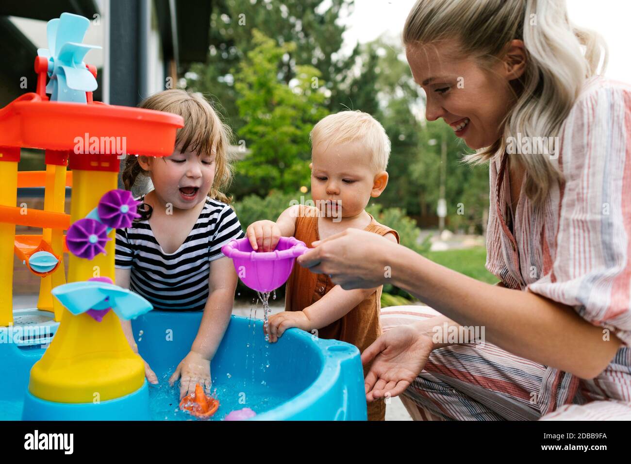 Mutter mit Kleinkind (18-23 Monate) Und Kleinkind Tochter (2-3) spielen mit Wasser im Garten Stockfoto