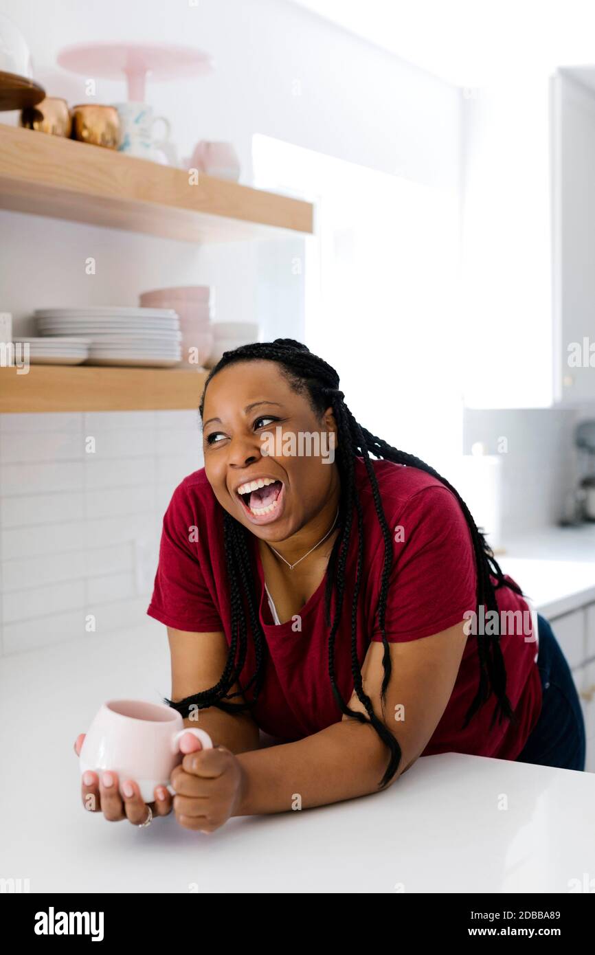 Lachende Frau, die sich auf die Küchentheke stützt Stockfoto
