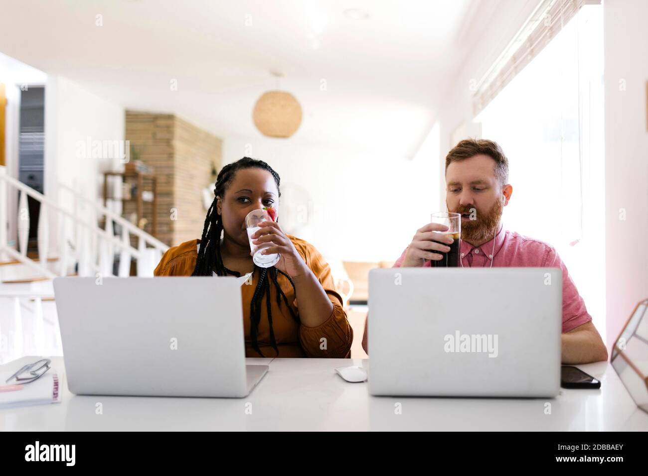 Mann und Frau trinken Wasser während der Arbeit mit Laptops an Heimbüro Stockfoto