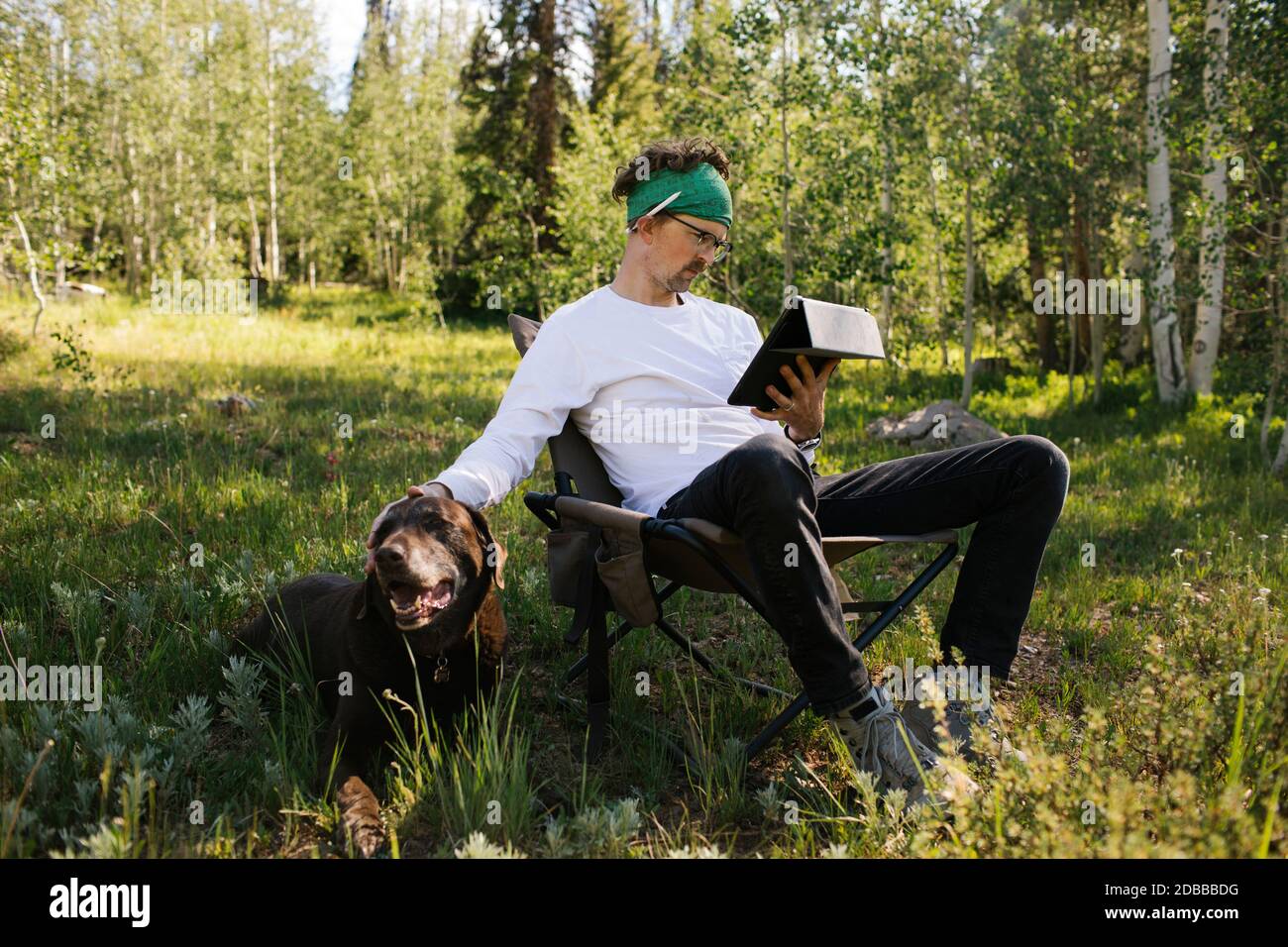 USA, Utah, Uinta National Park, Mann mit Hund sitzt auf der Wiese im Wald, mit Tablet Stockfoto