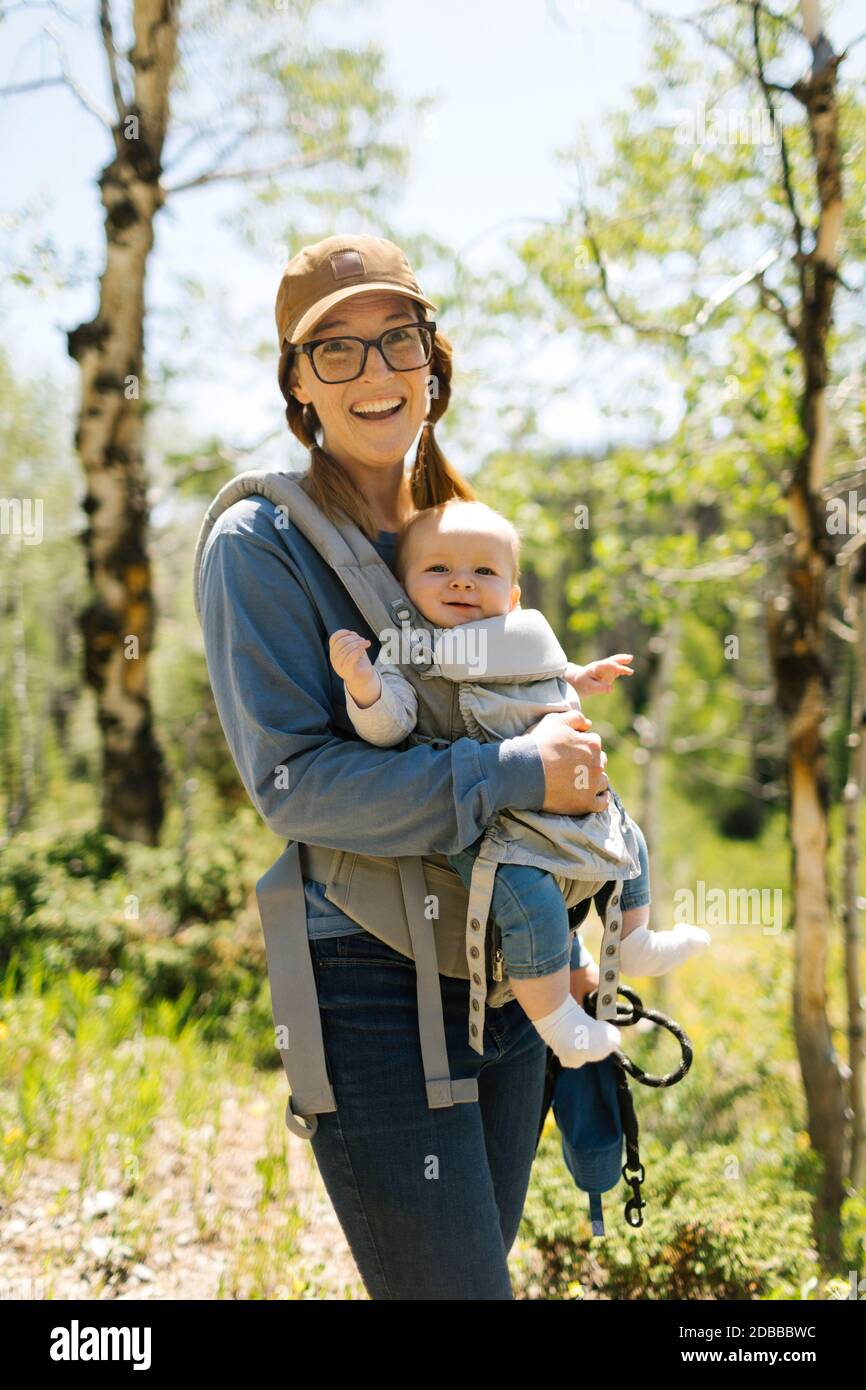 USA, Utah, Uinta National Park, Portrait einer lächelnden Frau mit Baby-Sohn (6-11 Monate) in Babytrage im Wald Stockfoto