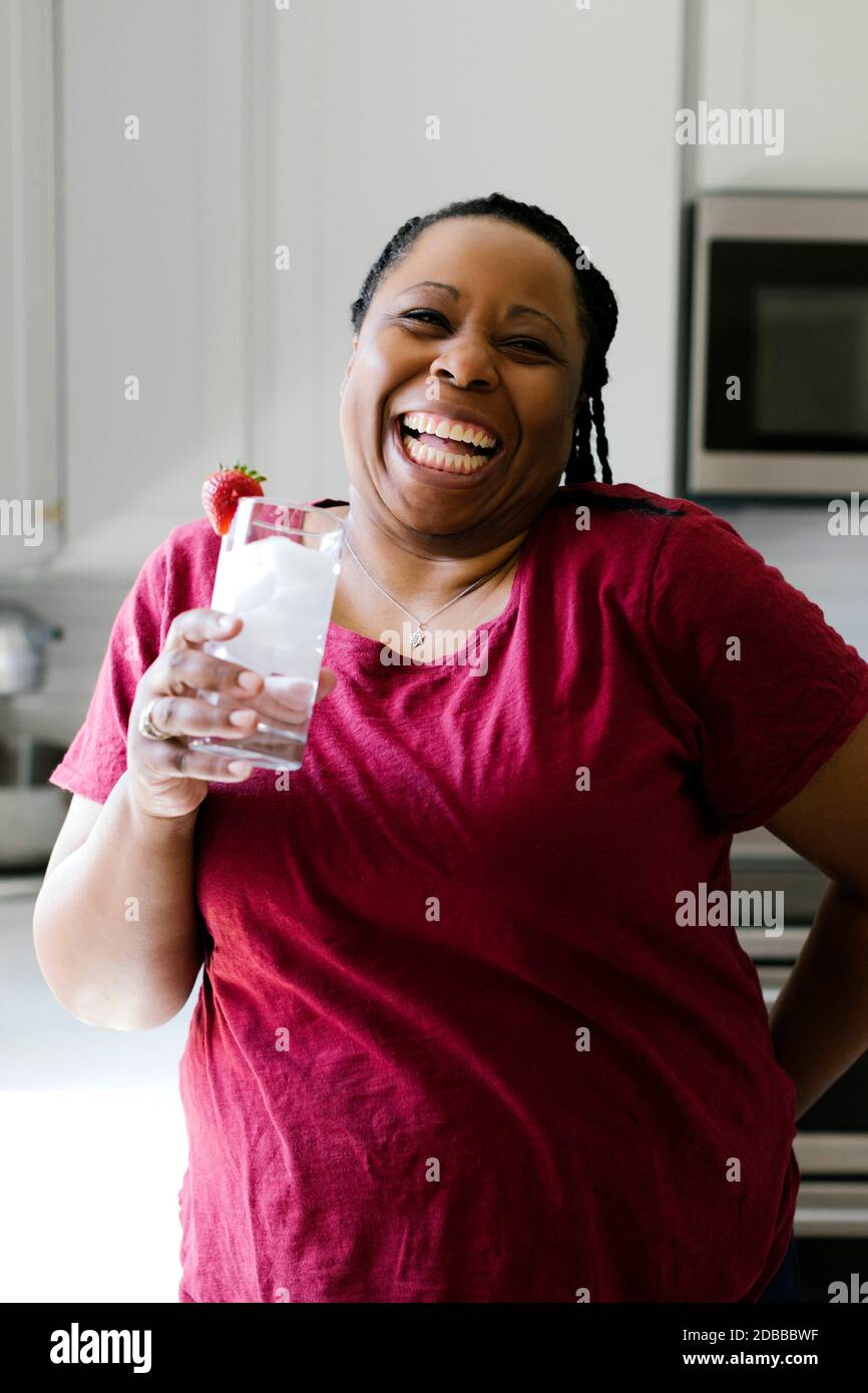Portrait der lächelnden Frau in lila Kleid hält Glas Wasser Stockfoto
