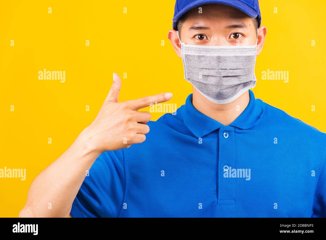 Asiatische junge Lieferung Arbeiter Mann in blauen T-Shirt und Mütze Uniform tragen Gesichtsmaske Schutz verwenden Finger zeigen er Gesichtsmaske unter Coronavirus oder COV Stockfoto