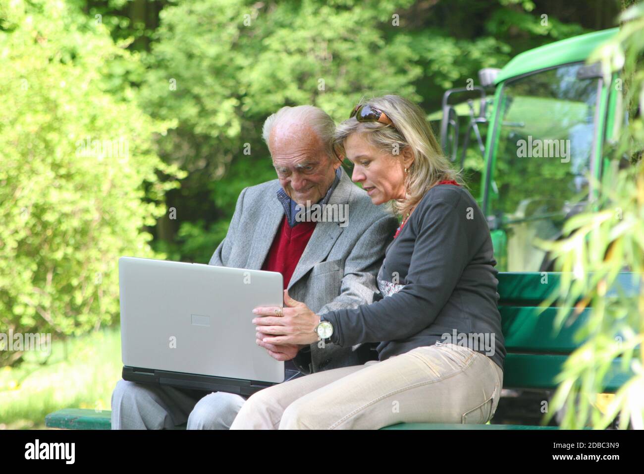 Glücklicher 90-jähriger Mann und junge Frau, die im Park am Laptop arbeiten Stockfoto
