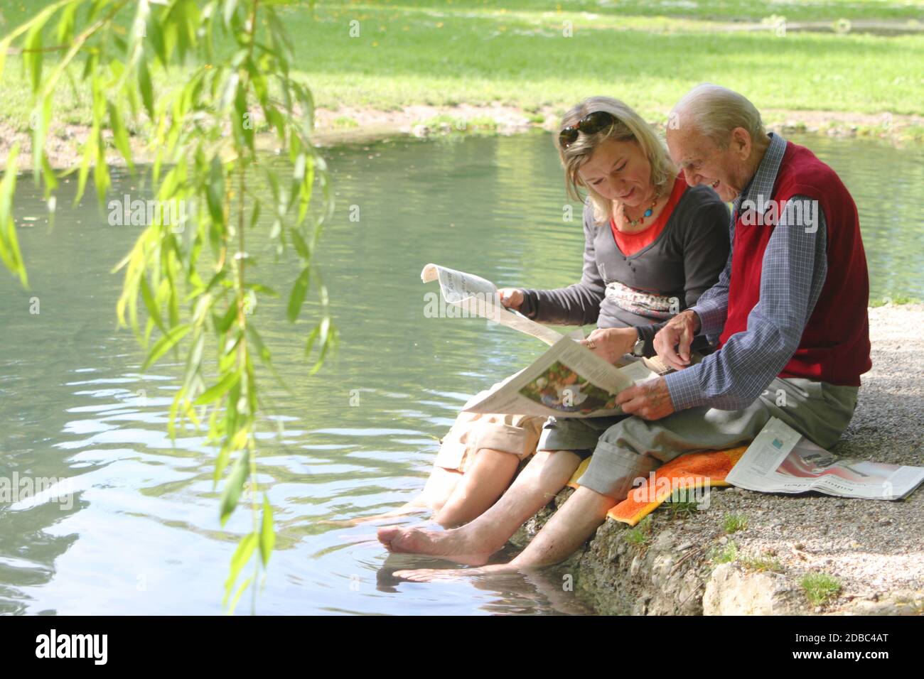 Glücklicher 90-jähriger Mann und junge Frau beim Zeitungslesen in der Natur Stockfoto