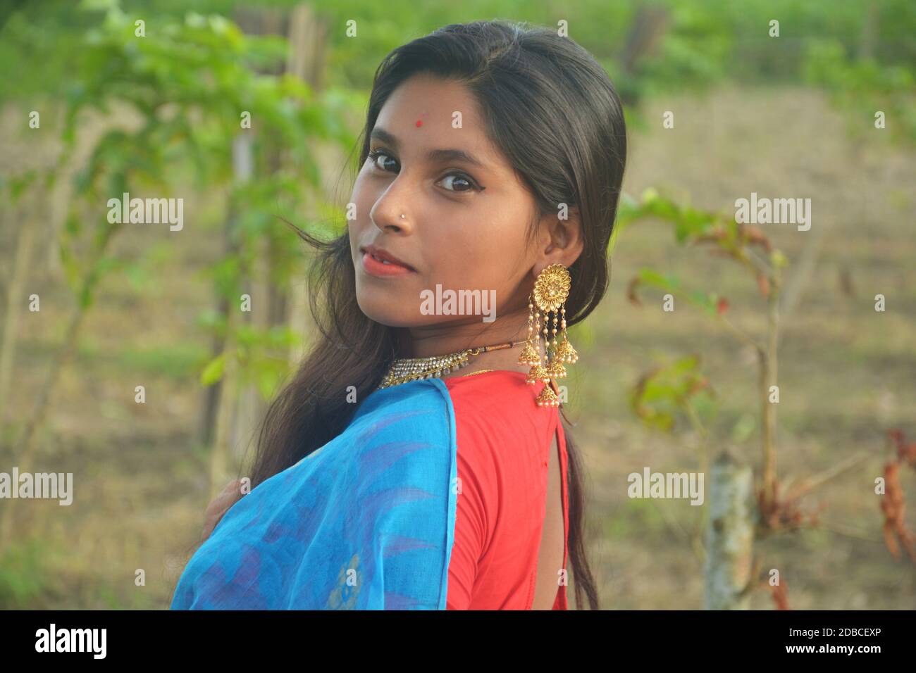 Nahaufnahme eines indischen bengalischen lächelnden Teenager-Mädchen mit langen dunklen Haaren goldfarben tragen Ohrringe und Halskette mit einem roten Bindi auf der Stirn, Stockfoto