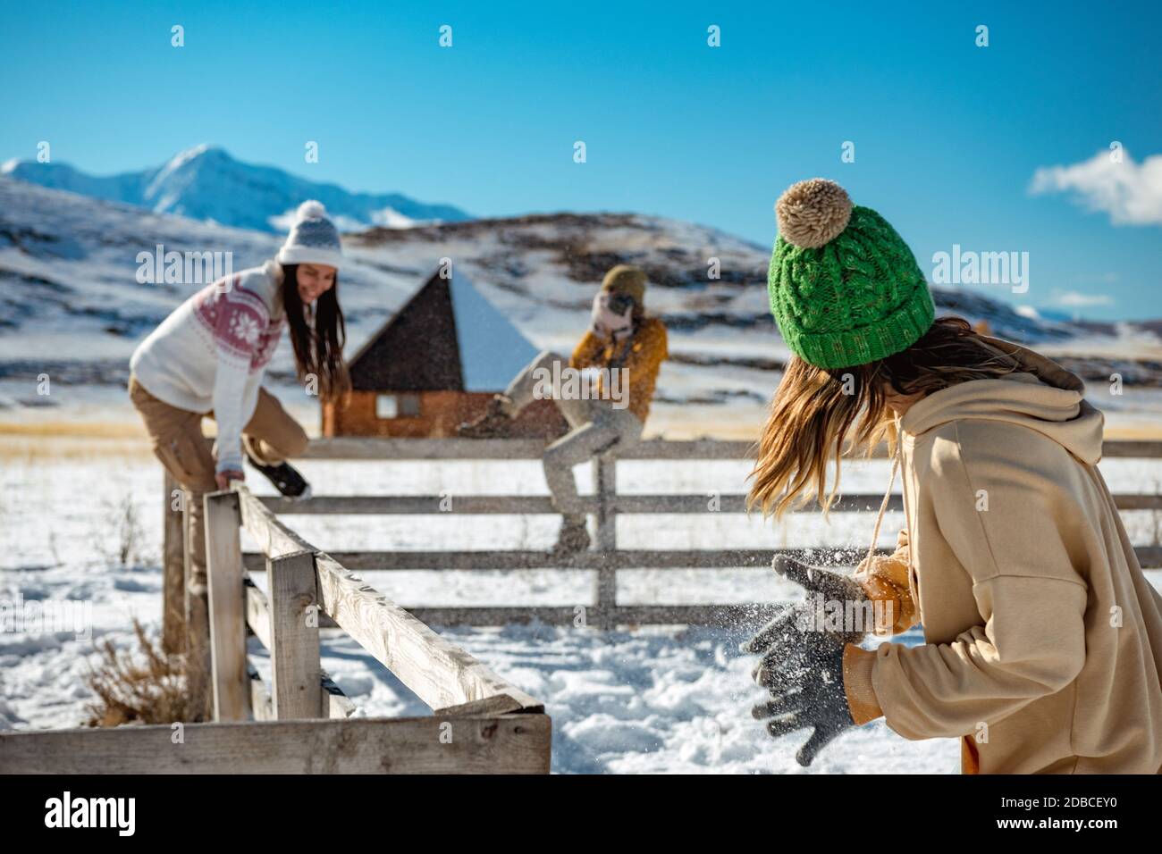 Drei glückliche junge Freundinnen haben Spaß am Holzzaun im Winter im Freien in den Bergen. Winterurlaub Konzept Stockfoto