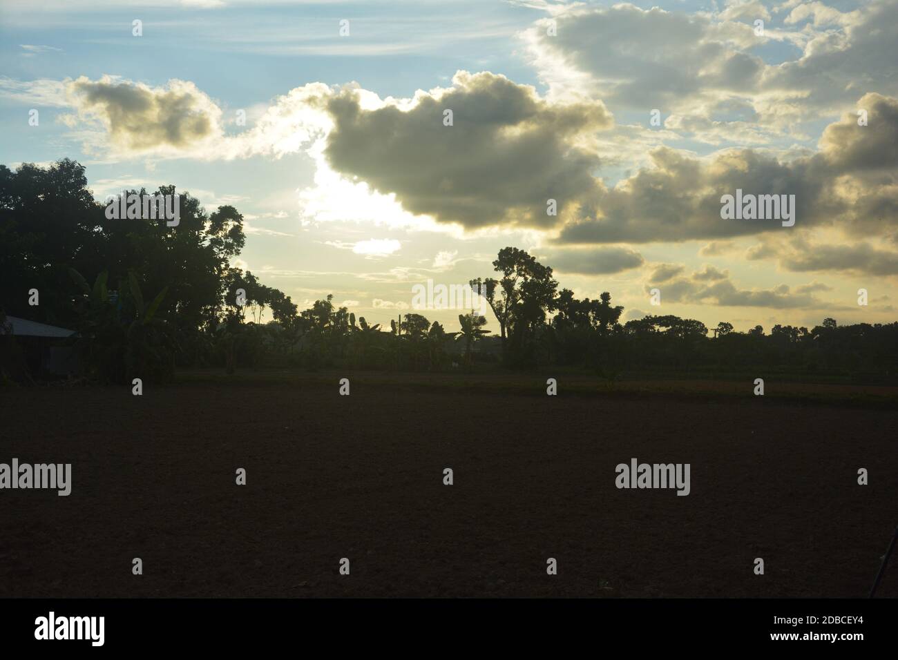 Die Szene eines Dorffeldes mit blauem Himmel und Sonne hinter den Wolken Stockfoto