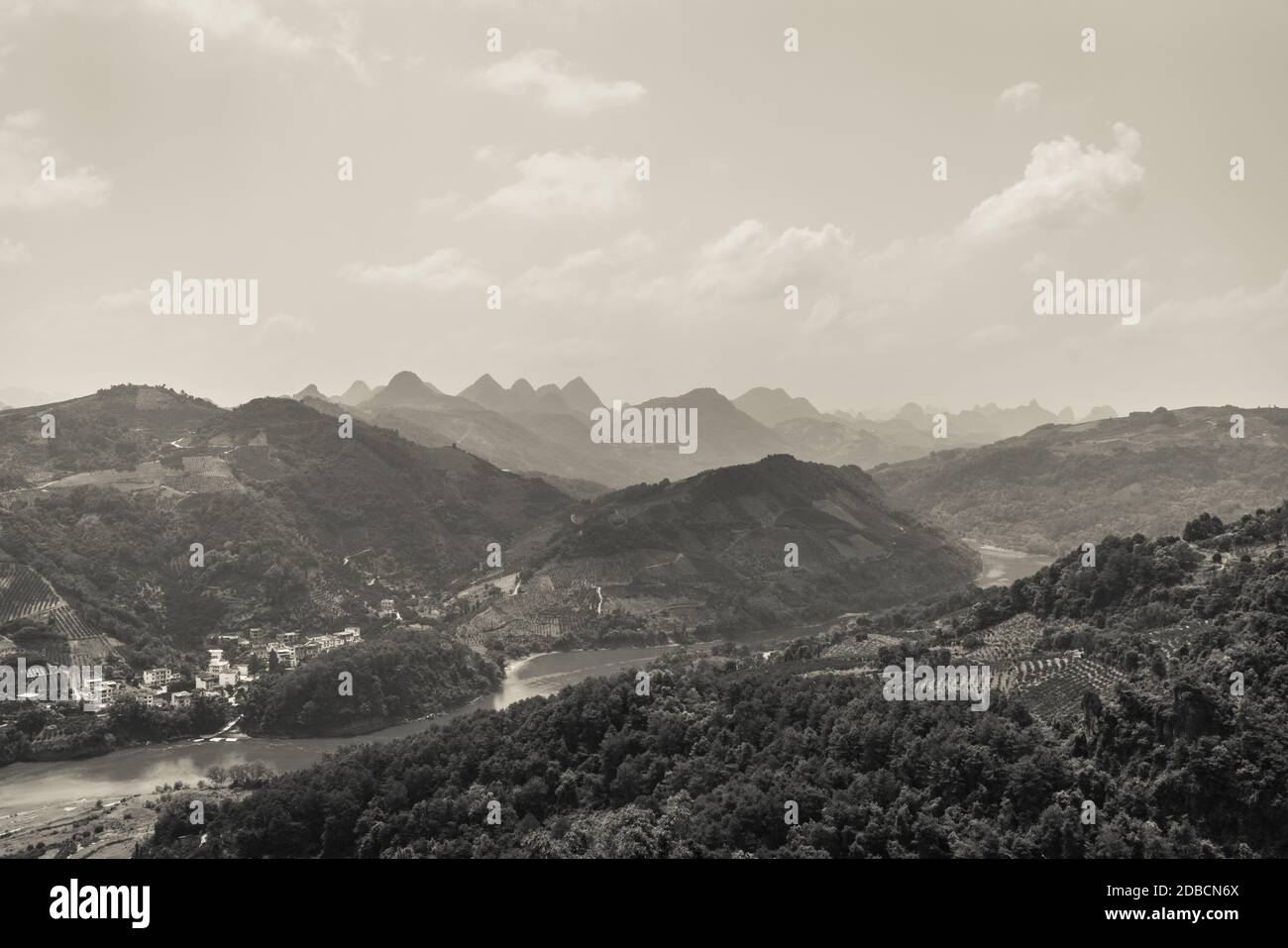 Eine Graustufenaufnahme einer schönen kleinen Stadt in den Hügeln am Fluss, aufgenommen von der Spitze eines Xianggong-Hügels, Karstgebirgslandschaft, Yangshuo, G Stockfoto