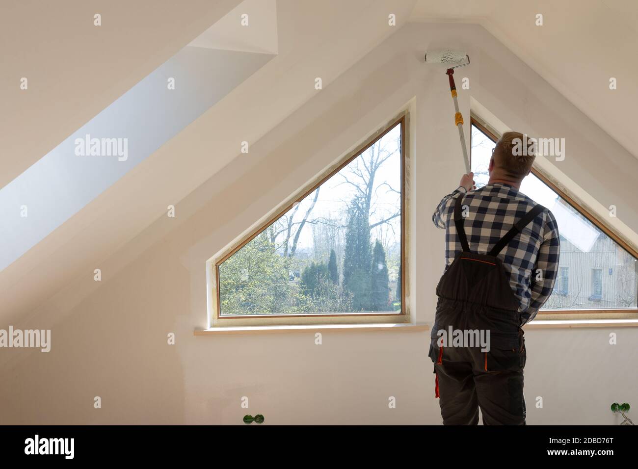 Hausbau Konzept, Handwerker Malerei eine Wand mit einer weißen Farbe in der Nähe Dachfenster im Dachgeschoss Stockfoto