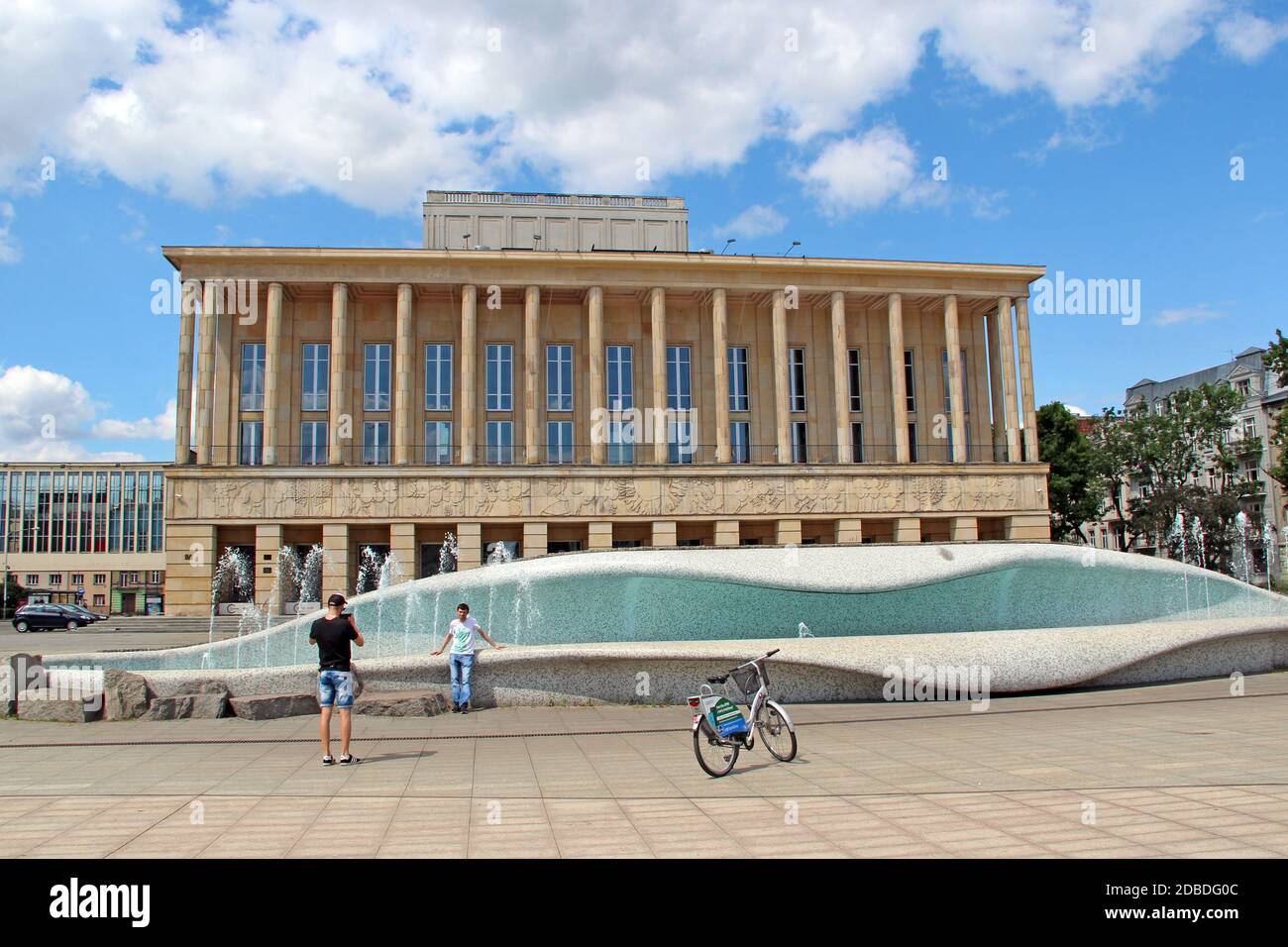 Junge Jungs Touristen fotografieren vor dem Hintergrund der Brunnen in der Nähe des Theaters in Lodz. Touristen machen Fotos auf dem Hintergrund des Theaters in Lodz verlassen die Stockfoto