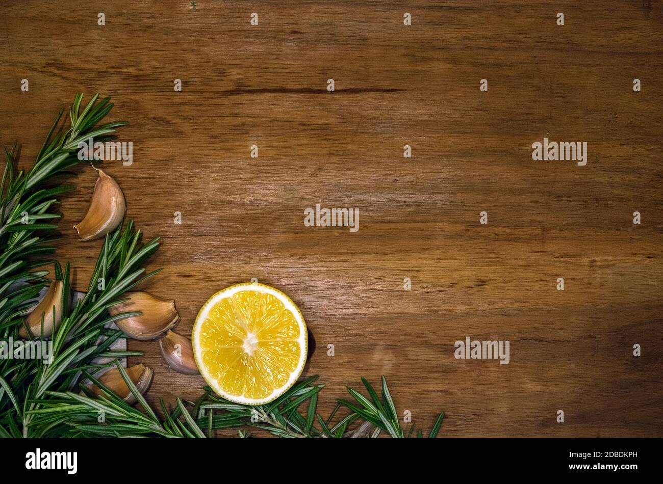 Frische Rosmarinzweige, Knoblauchzehen und Zitronenhälfte auf einem dunklen Holzbrett, Postkarte oder Einladungsvorlage Stockfoto