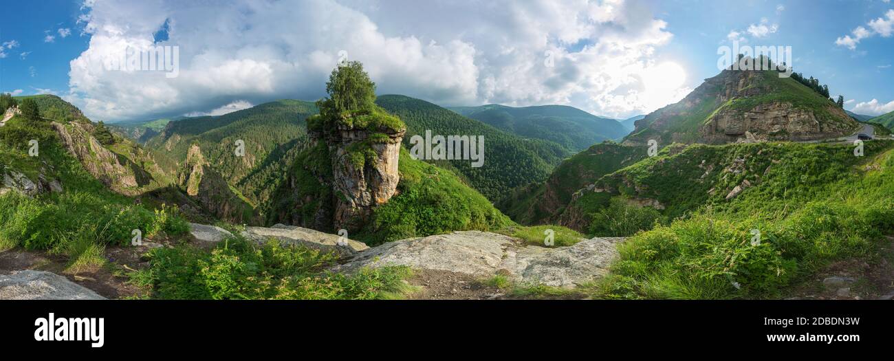 Wunderbarer Panoramablick auf majestätische sonnige Landschaft mit bewaldeten Bergklippen und bunten Himmel über dem märchenhaften Bergtal. Kaukasus, Russland Stockfoto