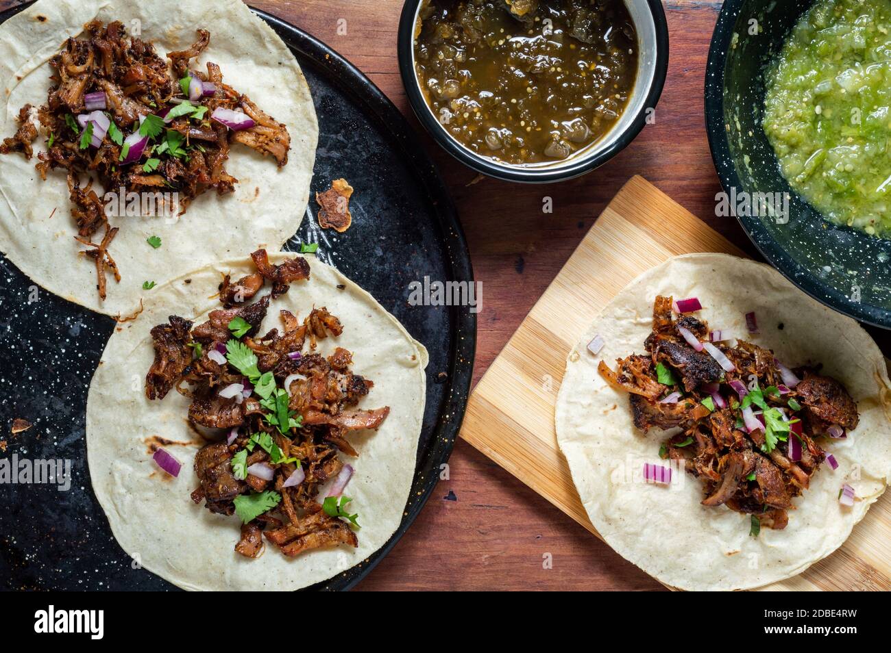 Carnitas Tacos mit roten Zwiebeln und roher Salsa verde. Mexikanische langsam gekochte Schweinefleisch Gericht aus Michoacan mit frischen grünen Salsa Stockfoto