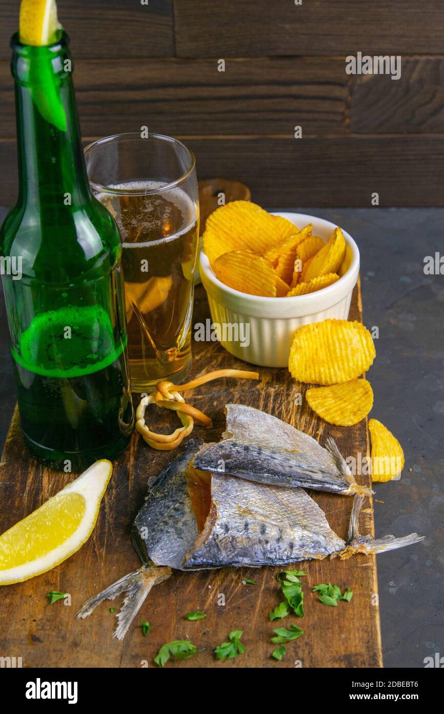 Getrocknete Brasse in Form eines Schmetterlings mit Bier, Zitrone und Kartoffelchips auf dunklem Holzbrett. Snack auf Fisch mit Bier. Nahaufnahme. Stockfoto