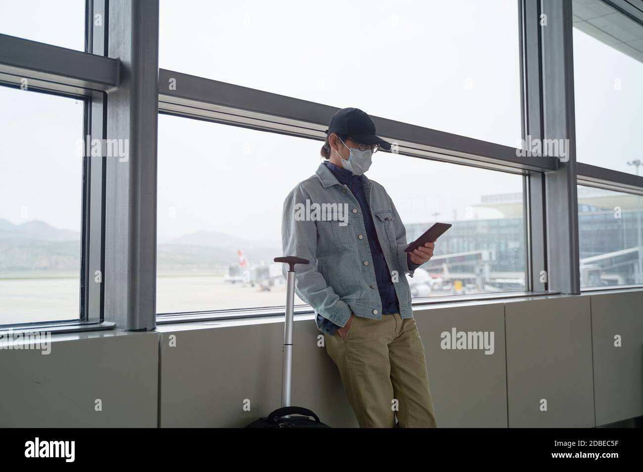 Junge asiatische Mann männliche Flugreisende Lesung e-Buch mit einem E-Reader beim Warten auf das Einsteigen im Flughafenterminal Stockfoto
