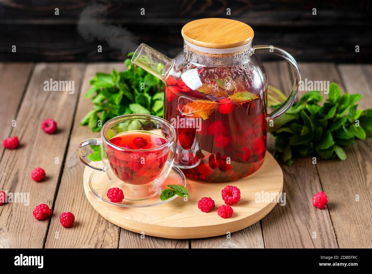 Kräutertee mit Beeren, Himbeeren, Minzblättern und Hibiskusblüten in Glas Teekanne und Tasse auf Holztisch Medizin für kaltes Vitamin Drink Rustikal Stockfoto