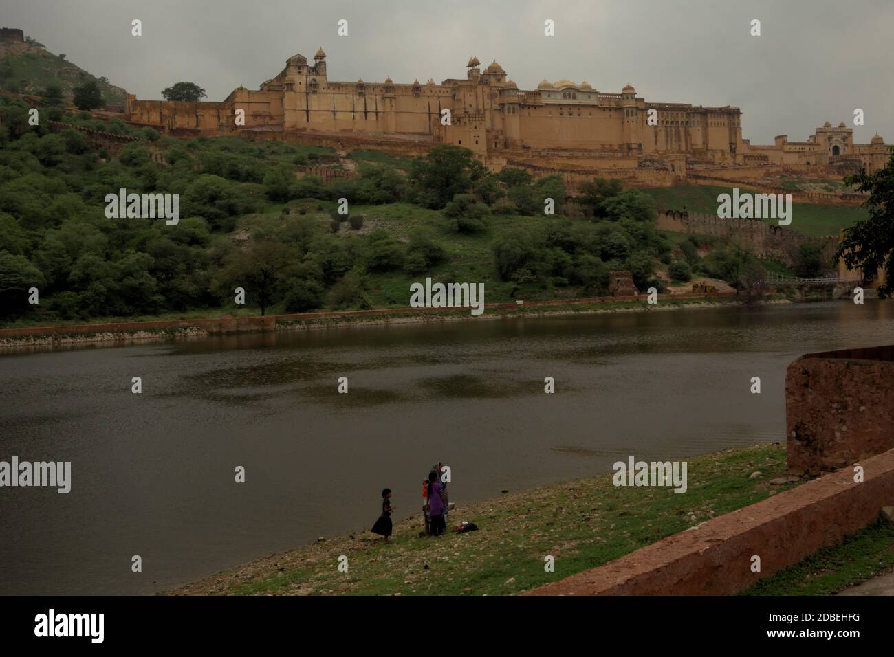 Frau und Kinder stehen auf der Seite des Maota Lake, mit Blick auf die historische Amer Fort in Amer, Rajasthan, Indien. Stockfoto