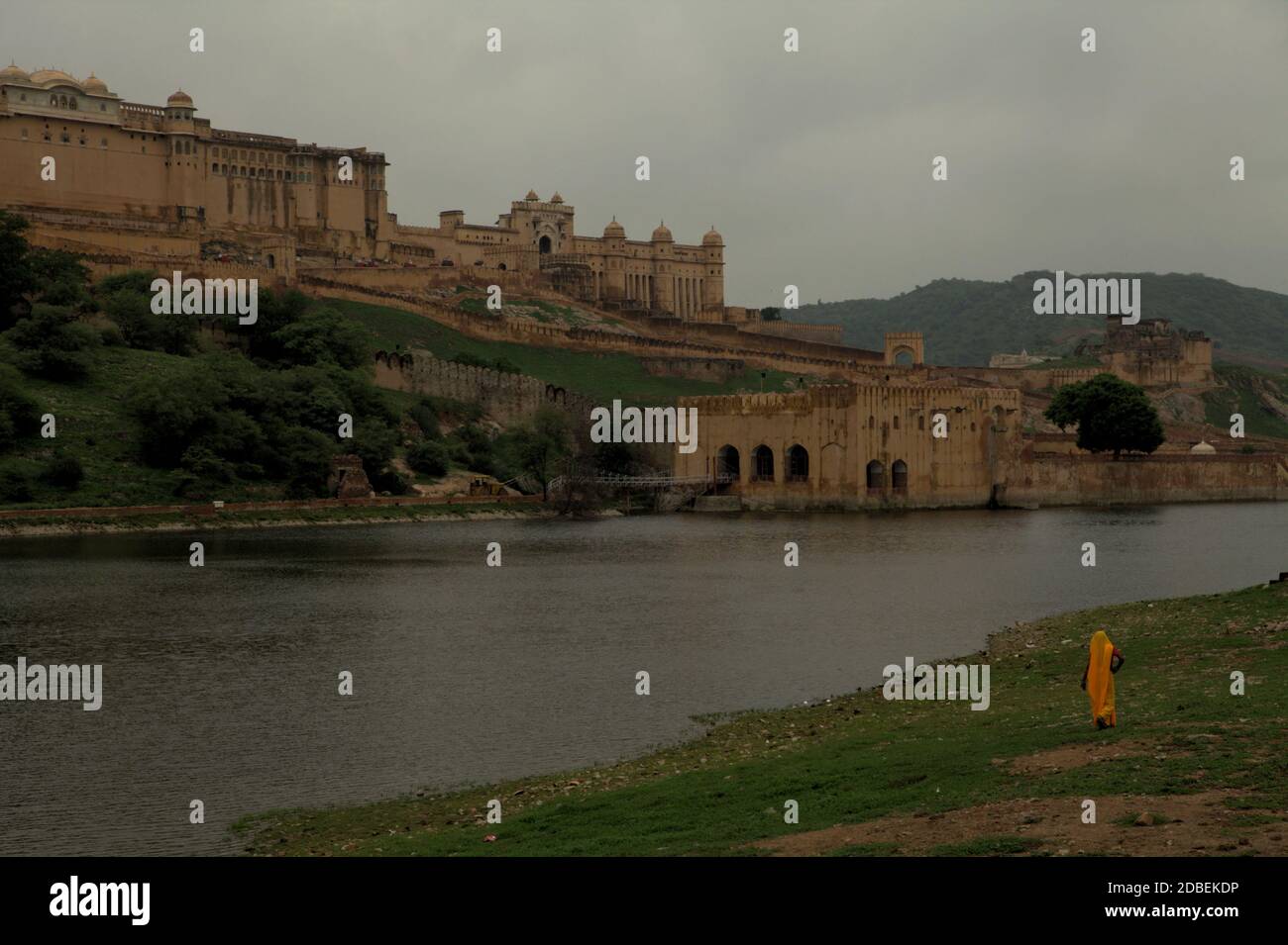 Eine Frau in Arbeitskleidung zu Fuß auf der Seite des Maota Lake, mit Blick auf die historische Amer Fort in Amer, Rajasthan, Indien. Stockfoto