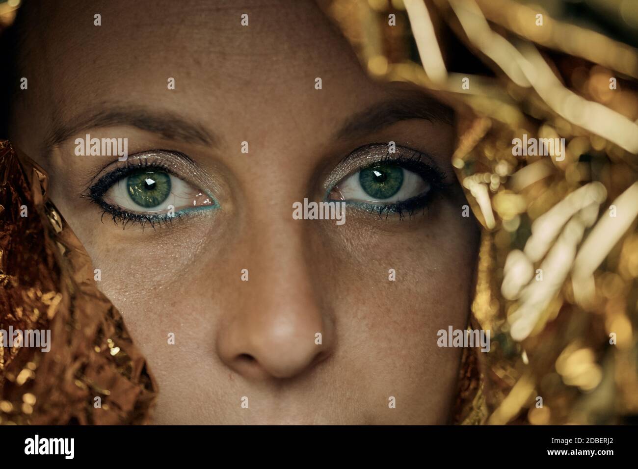 Nahaufnahme von ausdrucksstarken grünen Augen einer jungen Frau Gesicht mit Make-up und Goldfolie. Stockfoto