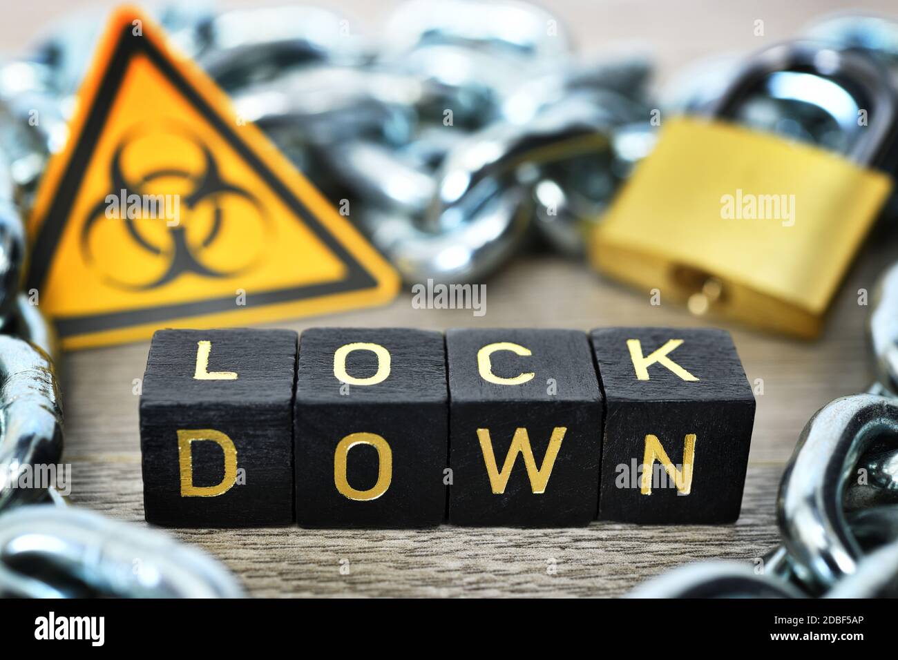 Buchstabenwürfel bilden das Wort Lockdown vor Biohazard Zeichen, Eisenkette und Vorhängeschloss, Corona Lockdown Stockfoto