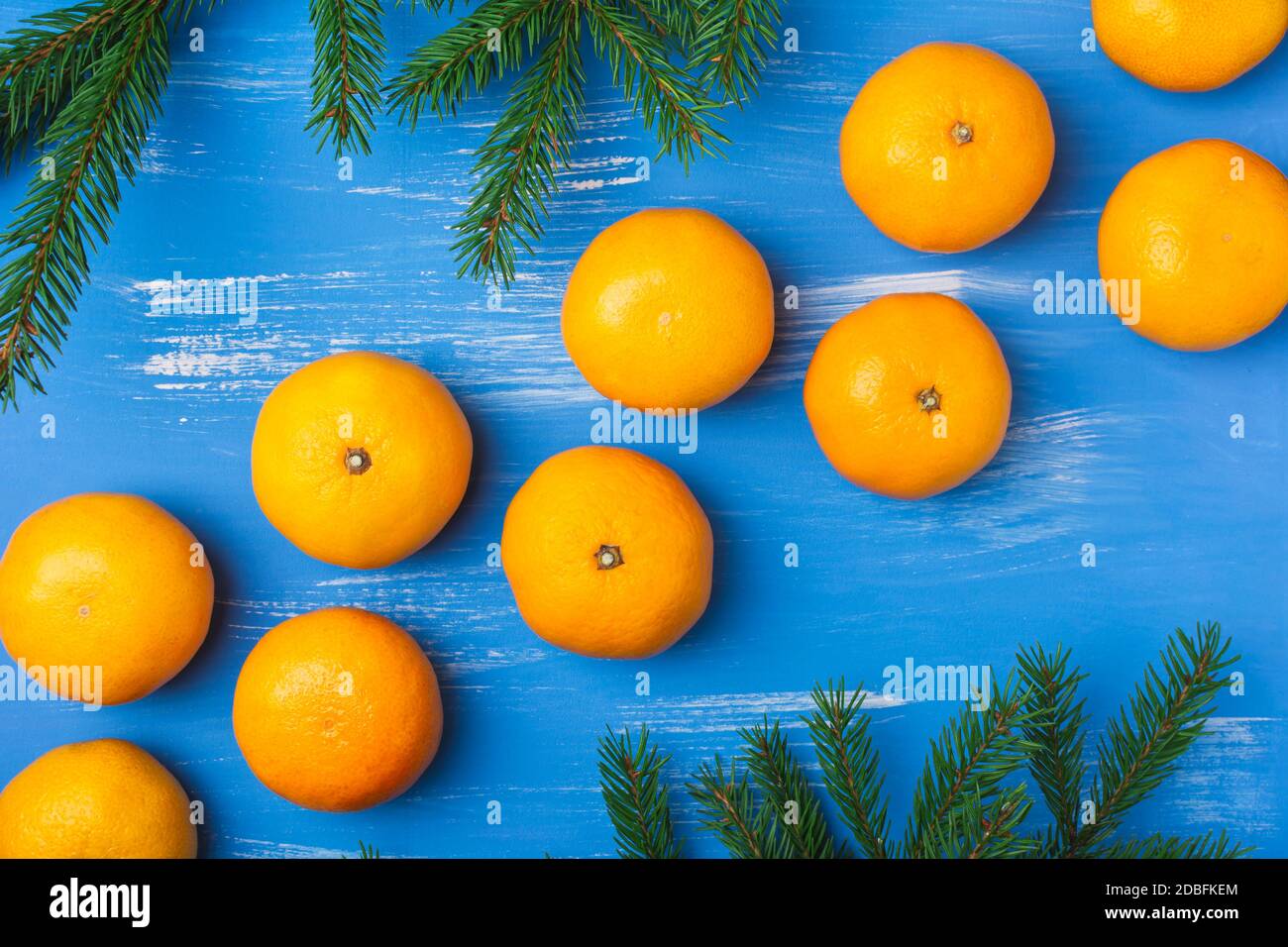 Mandarinen mit Tannenzweigen auf blauem Hintergrund. Postkarte Weihnachten und Neujahr. Diagonales Layout. Draufsicht Stockfoto