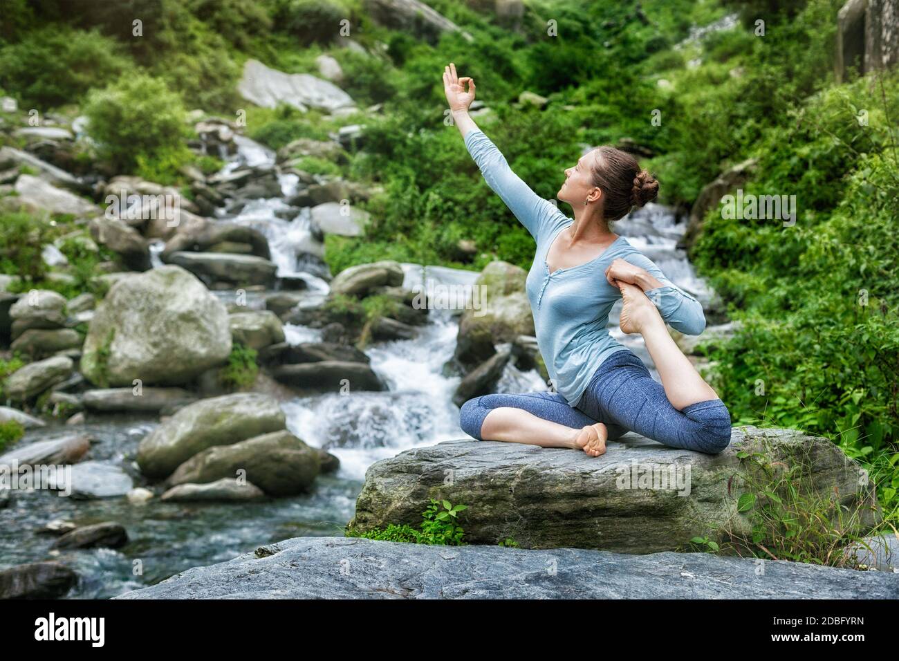 Junge sportliche fit Frau tun Yoga asana Eka pada rajakapotasana - einbeinige Königstaube Pose am tropischen Wasserfall Stockfoto