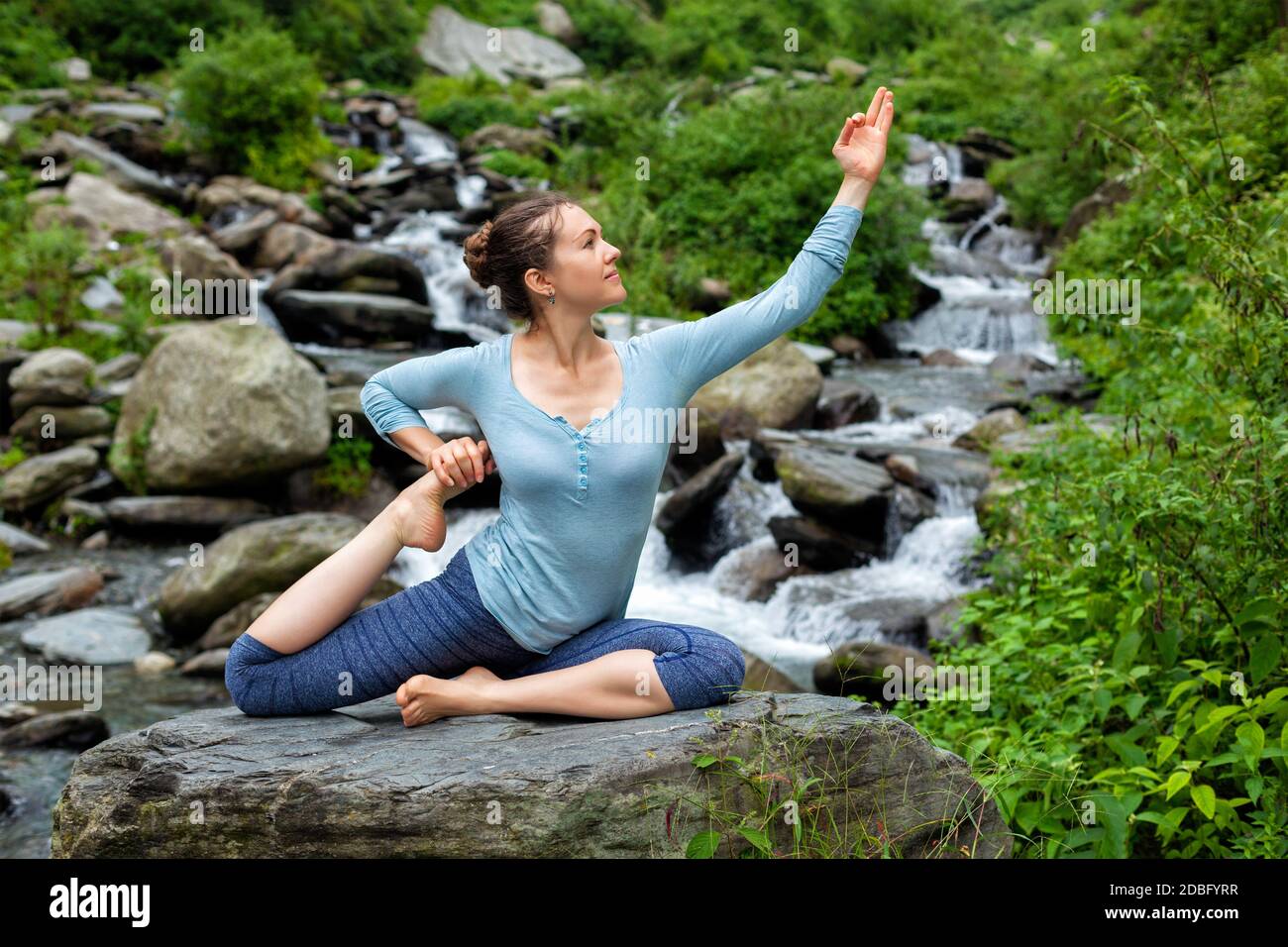 Junge sportliche fit Frau tun Yoga Asana Eka pada rajakapotasana - einbeinigen König Taube Pose bei tropischen Wasserfall. Himachal Pradesh, Indien Stockfoto