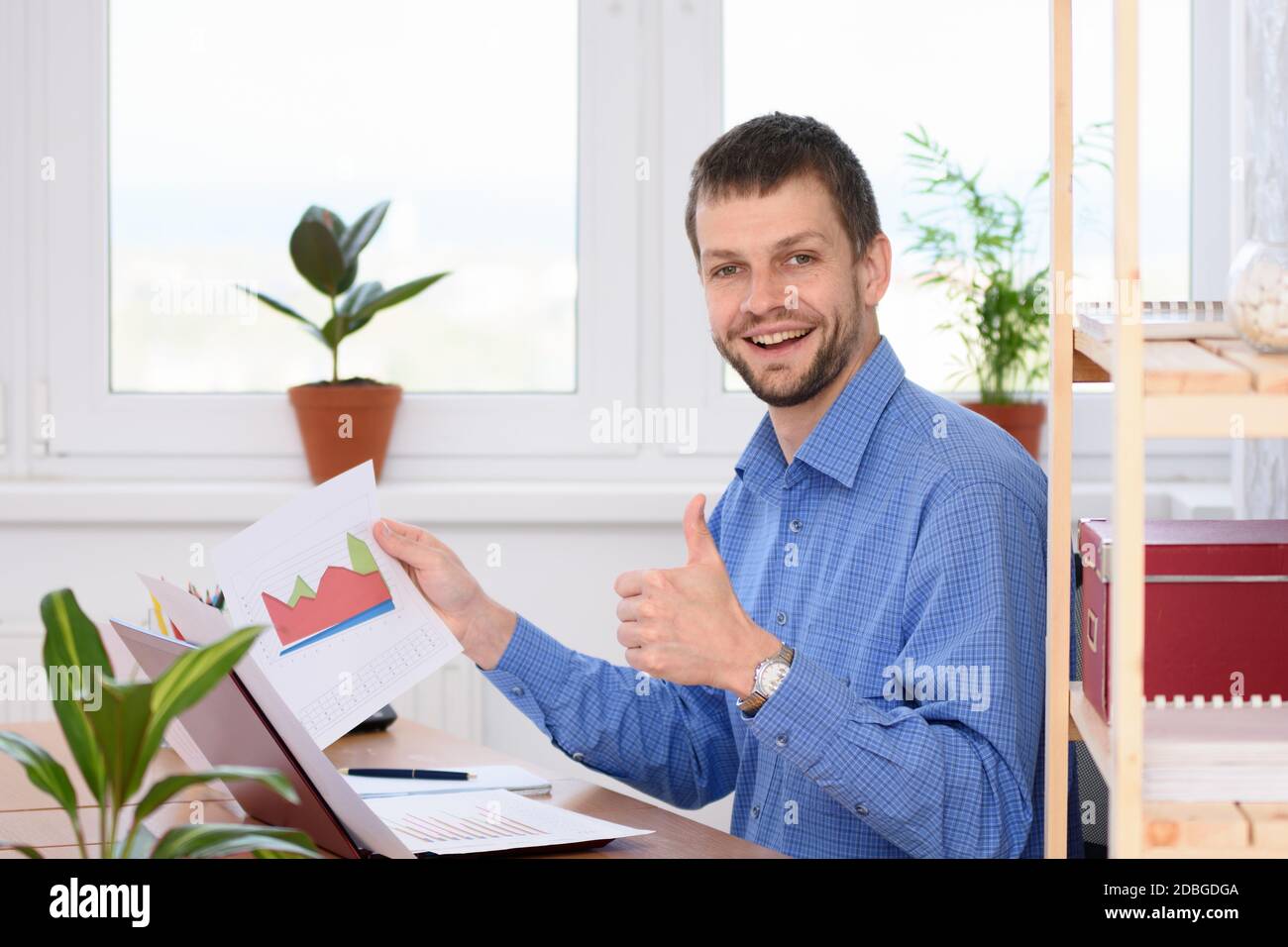 Junger Geschäftsmann zeigt Charts und Daumen hoch Stockfoto