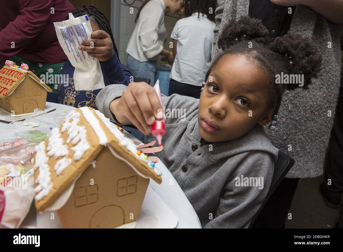 Unterprivilegierte Kinder bauen und dekorieren Lebkuchenhäuser auf einer Weihnachtsfeier in einem Gemeindezentrum in Manhattan, New York City. Stockfoto