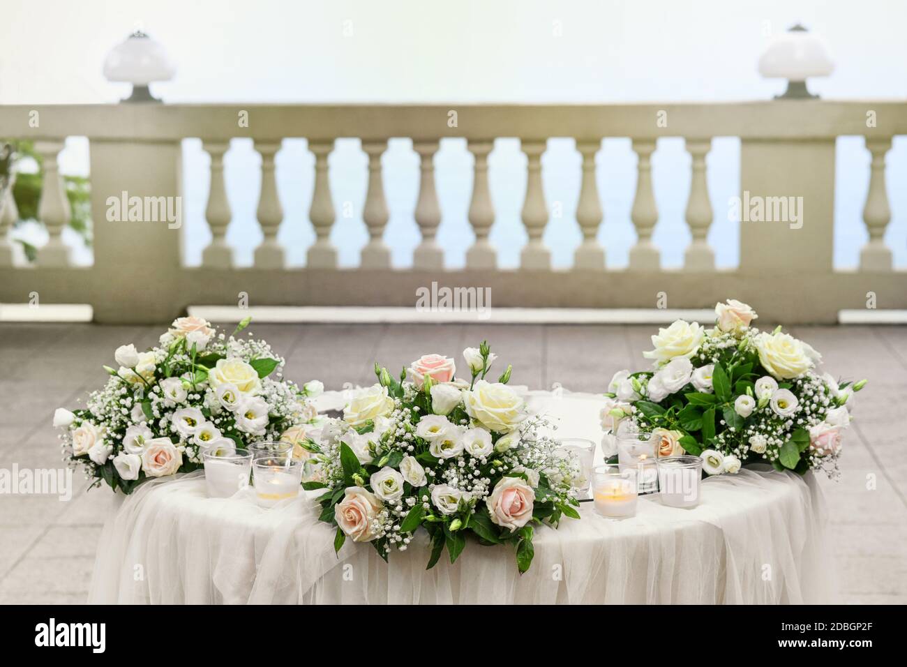 Elegante Outdoor-Hochzeitstisch mit drei Positionen von rosa gesetzt Und weiße Blumen und Kerzen auf einer Terrasse im Freien Mit Geländer Stockfoto