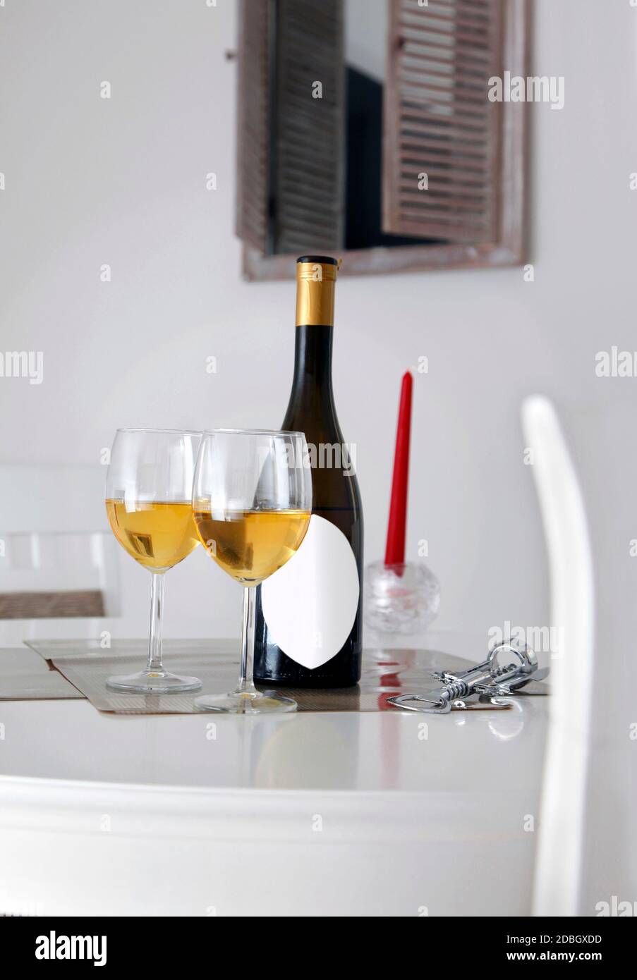 Flasche Wein mit weißem Etikett für Beschriftung, Öffner, zwei Gläser Weißwein auf dem Tisch und Fenster im Hintergrund Stockfoto Flasche Wein mit weißem Etikett für Beschriftung, Öffner, zwei Gläser Weißwein auf dem Tisch und Fenster im Hintergrund Stockfoto