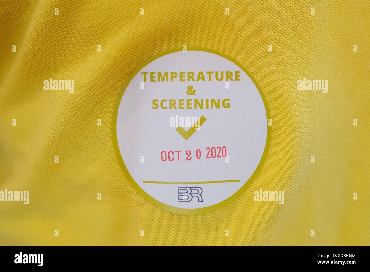 Nahaufnahme eines Aufklebers auf einem gelben Hemd mit der Aufschrift "Temperatur und Screening" mit dem Datum 20. Oktober 2020, Teil eines Covid-19-Arbeitsscreenings mit Temperaturkontrollen auf der Bishop Ranch, San Ramon, Kalifornien, 20. Oktober 2020. () Stockfoto