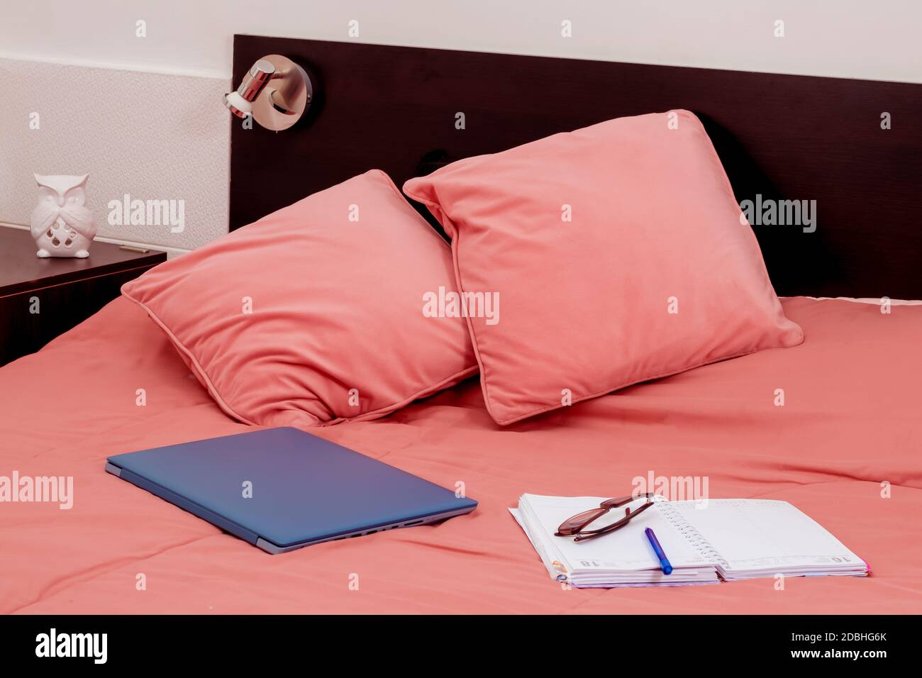 Geschlossener Laptop, Tagebuch und Gläser auf einem Bett im Schlafzimmer. Ich arbeite von zu Hause aus, eine bequeme Form der Kommunikation oder Unterhaltung. Aktuelles Konzept der Arbeit Stockfoto