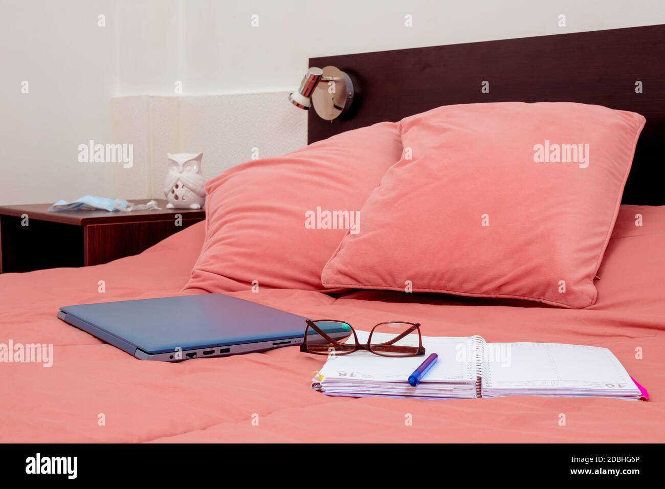 Geschlossener Laptop, Tagebuch und Gläser auf einem Bett im Schlafzimmer. Ich arbeite von zu Hause aus, eine bequeme Form der Kommunikation oder Unterhaltung. Aktuelles Konzept der Arbeit Stockfoto