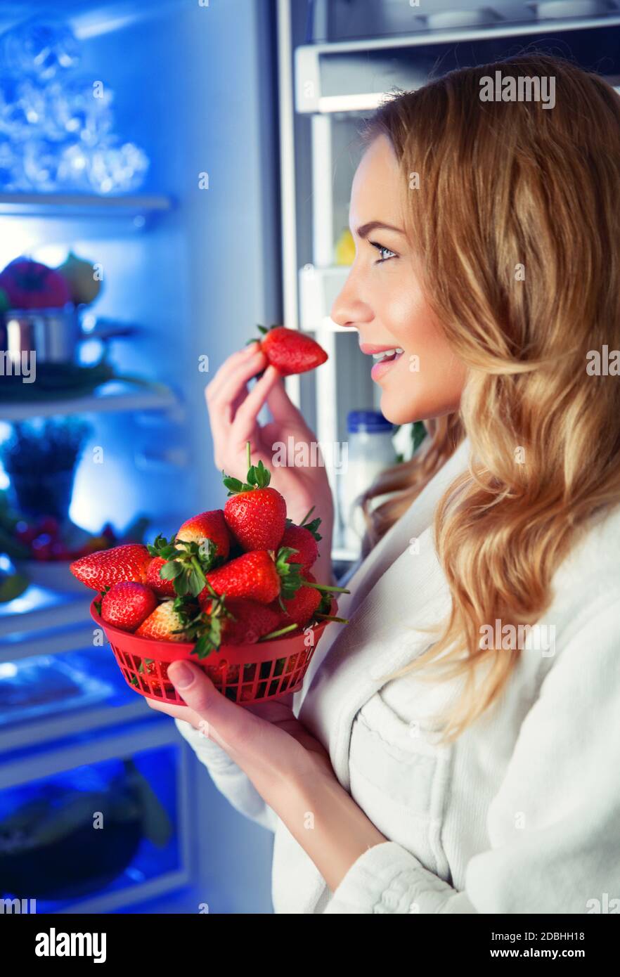 Porträt einer schönen blonden Frau mit Freude essen frische leckere Erdbeeren in der Nähe des offenen Kühlschrank, gute Auswahl, vegetarische Gerichte, Gewichtsverlust, Obst d Stockfoto