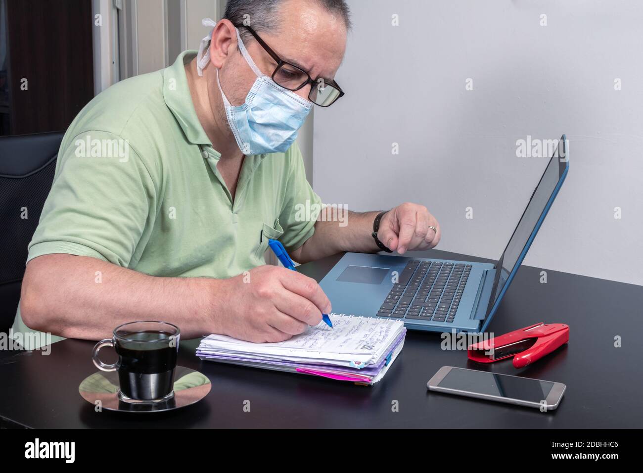 Mann, der von zu Hause aus mit einer Gesichtsmaske arbeitet. Arbeit von zu Hause Konzept, neue Normalität. Stockfoto